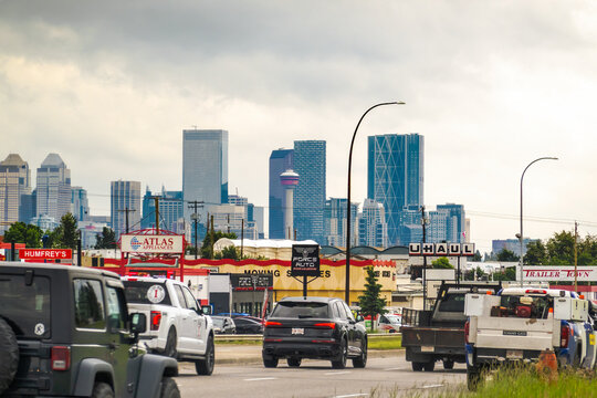 Calgary, AB, Canada. Sep 2, 2026. Vehicles driving through a commercial district with the downtown skyline and Calgary Tower behind.
