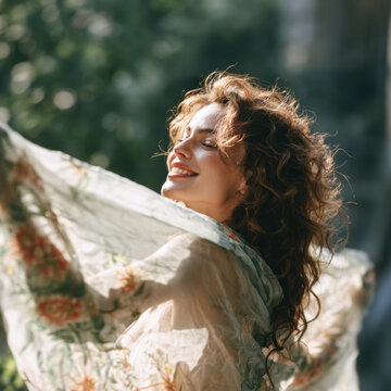Woman with curly hair holding a floral scarf outdoors in soft sunlight