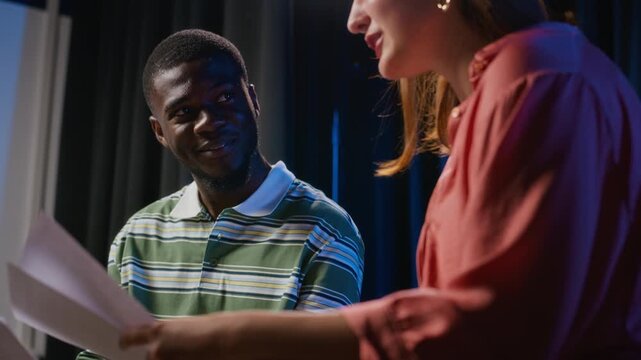 Young African American man discussing drama script with Caucasian woman during acting rehearsal. Footage fits performing arts education campaigns and theater workshops