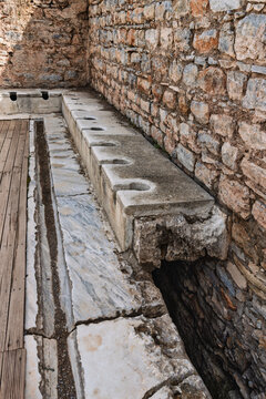 Ancient Roman public latrines in the archaeological site of Ephesus, Turkey, showing stone seats and drainage channels from the ancient city