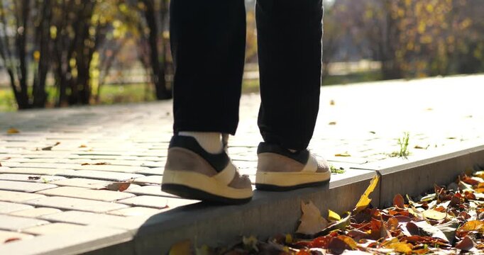 Close-up of walking feet on park path covered with autumn leaves. Warm sunlight and forward steps symbolize progress, freedom, journey, mobility and active outdoor lifestyle concept.