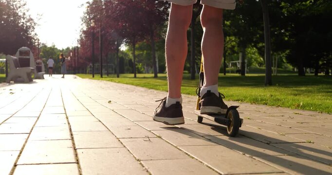 Child rides kick scooter along sunny park promenade. Young rider enjoys outdoor recreation on paved walkway. Active mobility scene shows freedom, exercise, and summer leisure in urban green space.