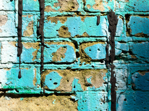 Weathered blue paint drips down brick wall