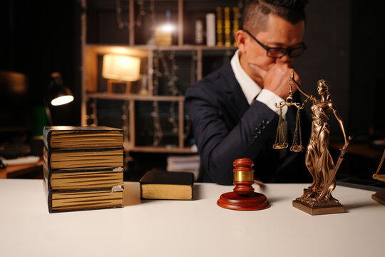 Pensive lawyer in thought behind Lady Justice statue, judge gavel, and stack of law books
