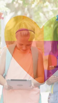 Animation of colourful puzzle pieces heart over school children using tablets