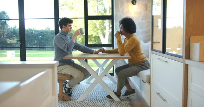 African American male partners holding hands, sitting in kitchen nook, sharing coffee