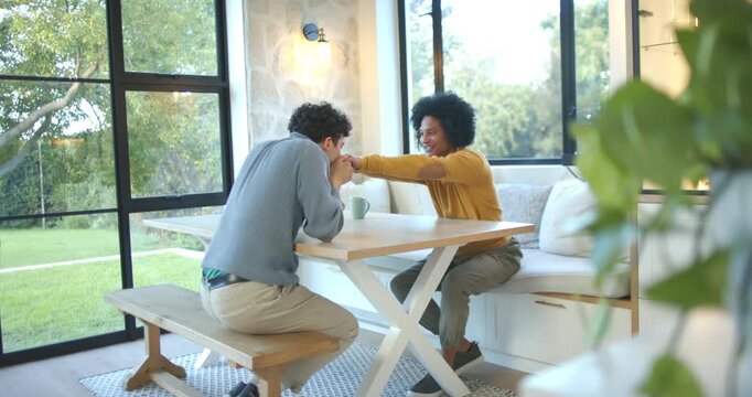 African American men holding hands, leaning in, pressing hand to face affectionately in dining nook
