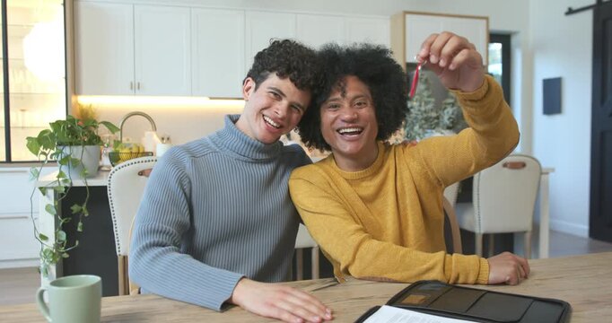 African American couple celebrating, raising red key fob after signing home papers at kitchen table