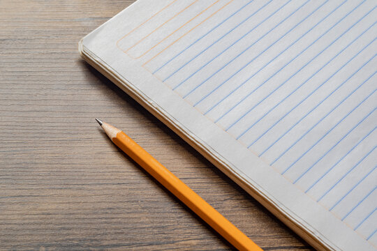 High angle view of yellow pencil and open blank lined notebook on wooden table with copy space
