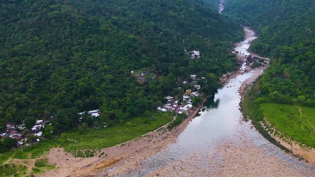 Dry piyain river through khasi hills with indigenous village houses and sandy riverbed at bichanakandi border area - aerial.