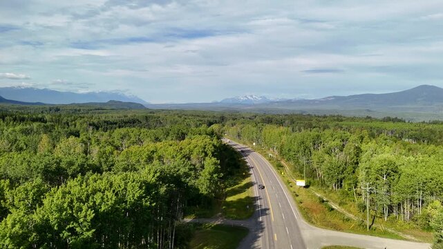 Aerial view of a winding road through a dense forest at New Hazelton, with mountains in the background, clear and balanced framing, natural lighting, evoking tranquility and vastness.