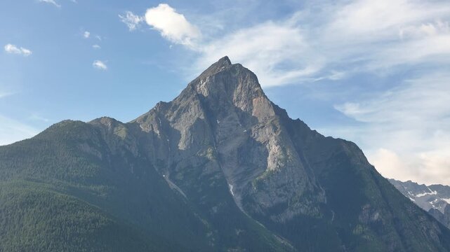 Aerial shot of a majestic mountain peak at New Hazelton, showcasing its rugged texture and expansive view under a clear blue sky with scattered clouds.