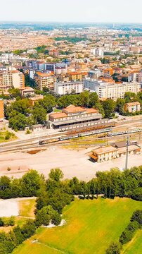 Vertical video. Modena, Italy. Modena Piazza Manzoni railway station, eclectic 1932 passenger building with Corinthian pilasters and curved pediment, bright summer sky. Drone footage, Point of intere