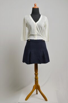 Broken white cropped button up cardigan with navy mini skirt displayed on a dress form
