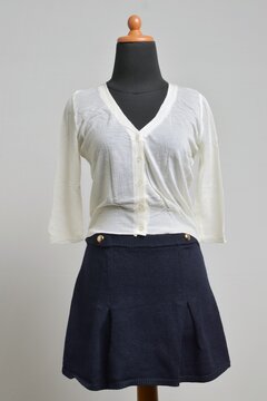Broken white cropped button up cardigan with navy mini skirt displayed on a dress form