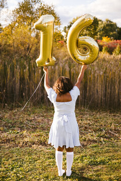 Teenage girl holding number sixteen balloons outdoors