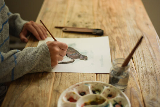 Person painting a watercolor turtle on a wooden table