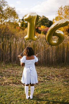 Teen girl from behind holding sweet sixteen balloons