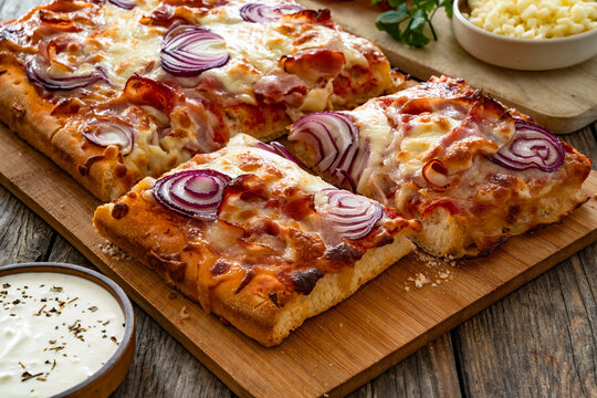 Pizza with bacon, mozzarella cheese and red onion on wooden table
