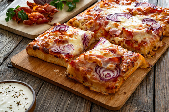 Pizza with bacon, mozzarella cheese and red onion on wooden table
