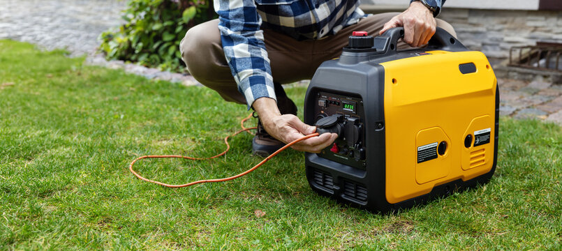 Man connecting cable to portable gasoline inverter generator outlet for home backup power or outdoor electricity supply
