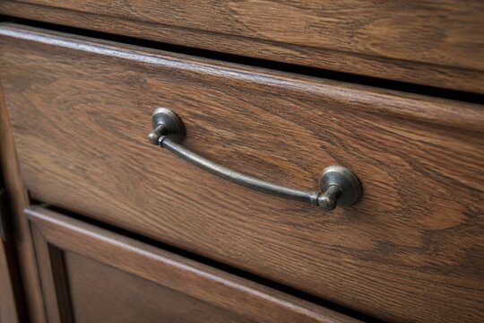 Close-up of a dark brown wooden drawer with an antique metal handle