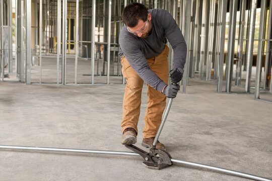 Electrician bending electrical conduit with a hand bender tool on a construction site