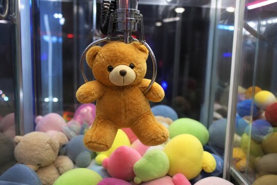 Arcade claw machine grabbing a brown teddy bear plush toy amidst other colorful toys