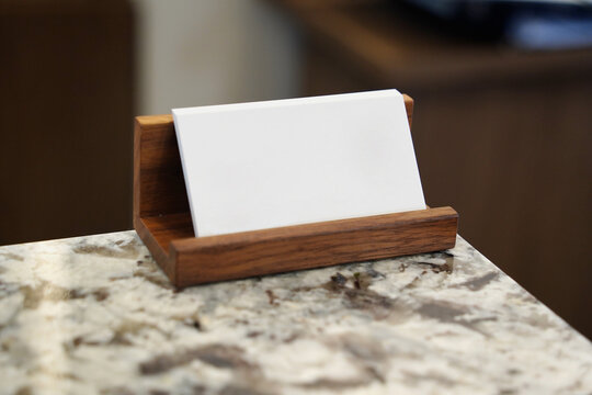 Blank white business card mockup on a wooden holder over marble desk