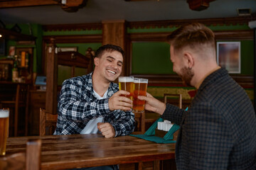 Two men clinking beer glasses at rustic pub wooden table