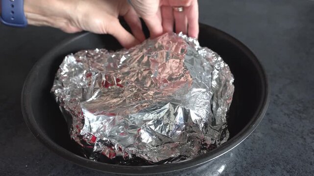 A woman's hands seal fish in foil for baking in the oven. View from above, close-up.