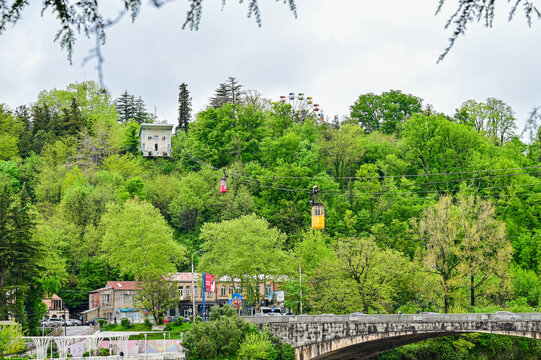 Historic cable car with a red cabin crossing a river bridge in the valley of the mining town of Chiatura, Imereti region, Georgia