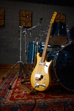 Bright yellow bass lying by drum set on decorative rug under atmospheric studio lighting