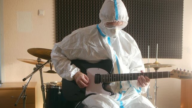 Musician in hazmat suit playing electric guitar in empty studio symbolizing isolation creative resistance. Surreal performance art. Guitarist in hazmat suit performing music in studio conceptual shoot