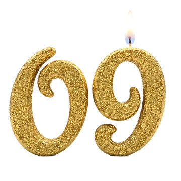 Sparkling gold glitter number sixty nine birthday candle with a burning flame isolated on a solid black background