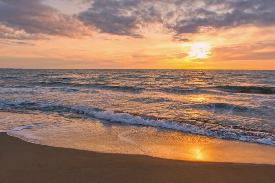 Colorful sunset viewed from the sandy sea beach with soft waves