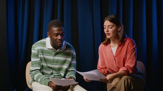 Young African American man and Caucasian woman rehearsing acting scene with scripts while camera zooms out. Video fits performing arts marketing, drama class promos, or theater education projects