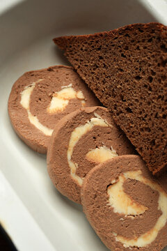 Liver pate roll with butter and dark rye bread in enamel dish close up