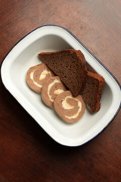 Liver pate roll with butter and dark rye bread in enamel dish close up
