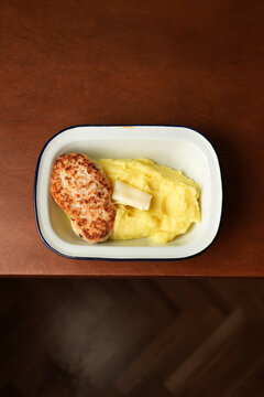 Fried chicken cutlet with mashed potatoes and butter in enamel dish close up