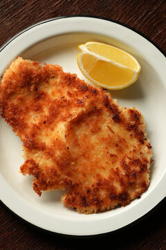 Crispy breaded schnitzel cutlet with lemon wedge on enamel plate flat lay