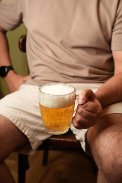 Man holding mug of cold draft lager beer seated indoors close up