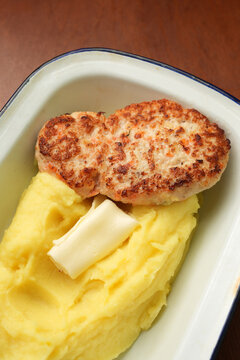 Fried chicken cutlet with mashed potatoes and butter in enamel dish close up