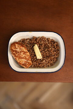 Fried chicken cutlet with buckwheat porridge and butter in enamel dish close up