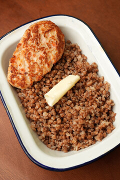 Fried chicken cutlet with buckwheat porridge and butter in enamel dish close up