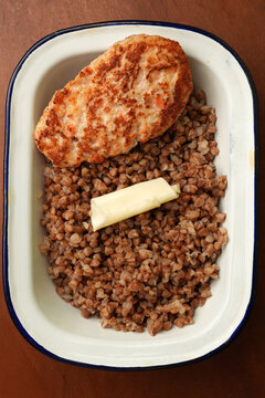 Fried chicken cutlet with buckwheat porridge and butter in enamel dish close up