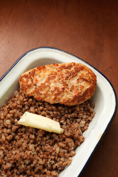 Fried chicken cutlet with buckwheat porridge and butter in enamel dish close up