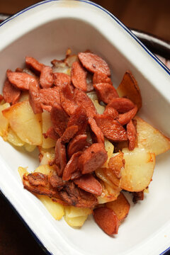 Pan-fried potatoes with smoked sausages in enamel dish flat lay