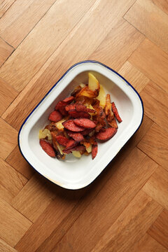 Pan-fried potatoes with smoked sausages in enamel dish flat lay