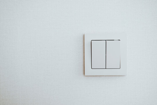 A light switch is mounted on a smooth, light-colored wall. The switch features two toggles arranged vertically and is set against a plain background